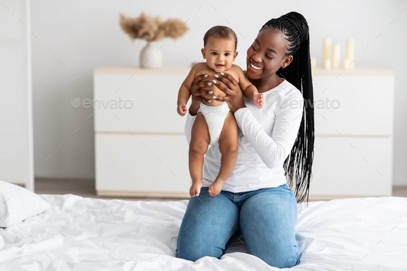 Black mom sitting on bed with her cute little baby - Stock Photo - Images