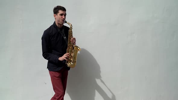Street Musician Is Playing Saxophone at White Wall Background Outdoors, Performing Melody and Song alt