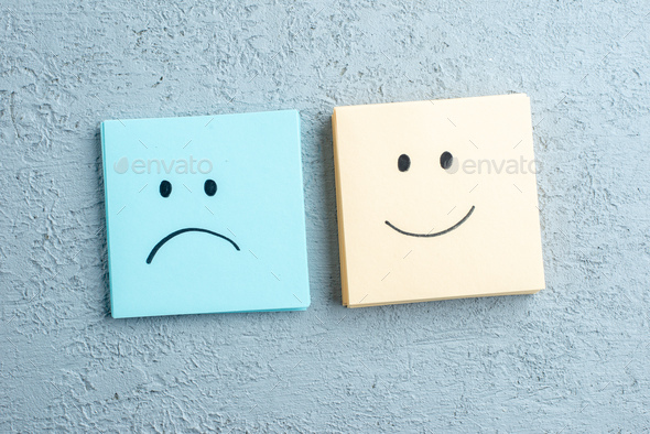 Front view of many sad and happy emoji faces drawings on small note sheets on gray distressed