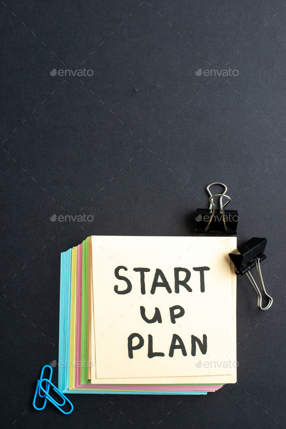Vertical view of START UP PLAN writing on small note sheets simple office tools on the bottom on