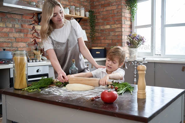 Loving mother teach her son to cook pizza in kitchen at home