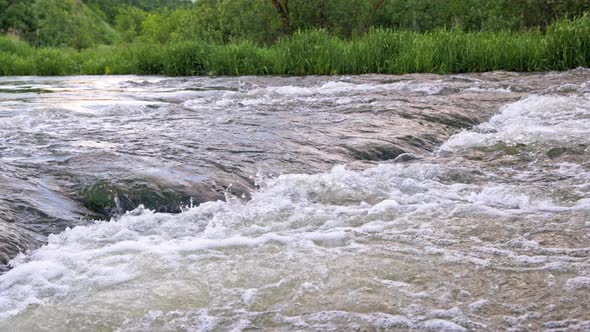 the Flowing Water of a Summer River with a Small Rapid Waterfall in Slow Motion at Daylight