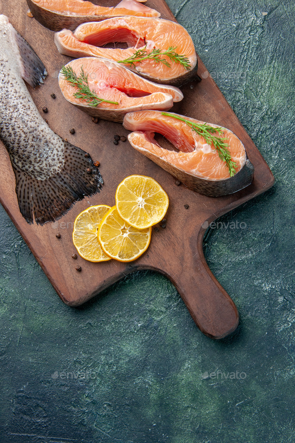 Top view of fresh raw fishes lemon slices greens pepper on wooden cutting board on dark background