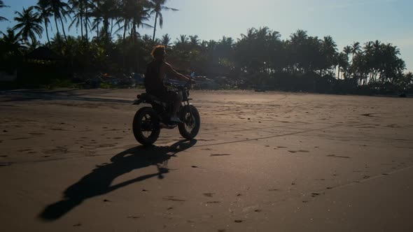 Biker Driving By Sand Shore Past Bungalows and Tropical Trees alt