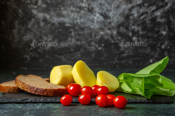Side view of fresh cut potatoes and dietary bread slices tomatoes green bundle on wooden cutting