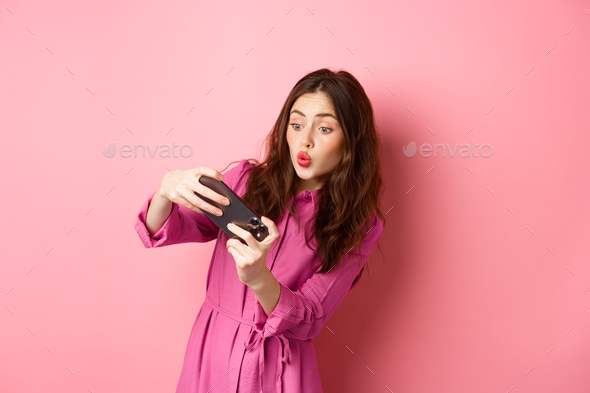 Technology concept. Carefree young woman tilt body, holding smartphone horizontally, playing video