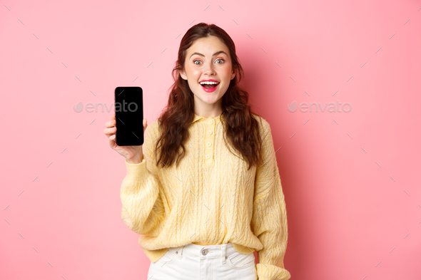 Technology and online shopping. Attractive woman student looks excited, shows empty smartphone