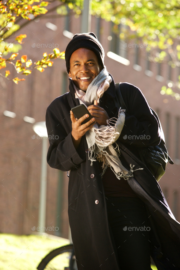 african american man walking in city with mobile phone and winter jacket