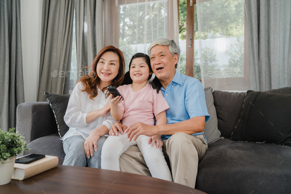 Asian grandparents watch TV with granddaughter at home. - Stock Photo - Images