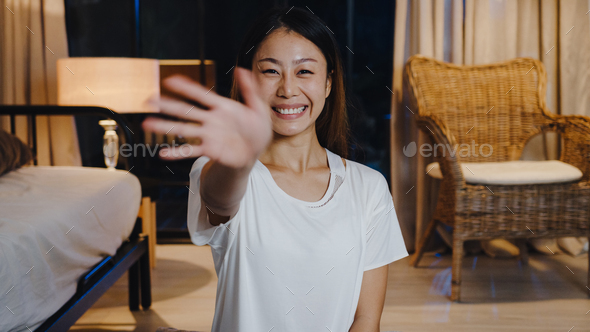 Cheerful young Asia lady vlogger look at camera using mobile phone talk video call in living room