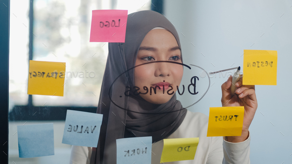 Asia muslim lady write information, strategy, reminder on glass board in new normal office.