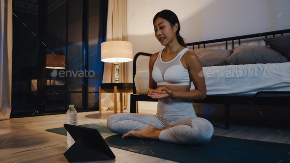 Young Asia lady doing work out and using tablet to watch yoga video tutorial at home night.