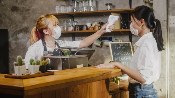 Young Asia female restaurant staff wearing face mask using infrared thermometer check before enter.