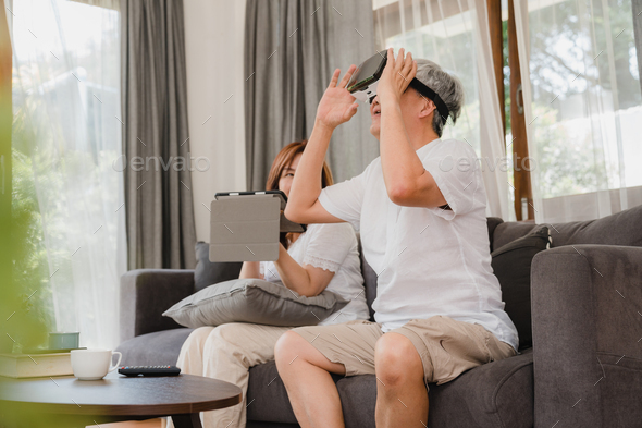 Asian elderly couple using tablet and virtual reality simulator playing games in living room.