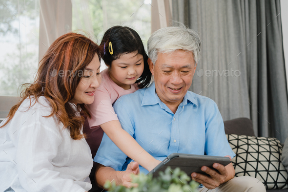Asian grandparents and granddaughter using tablet at home. Stock Photo by  Tirachard