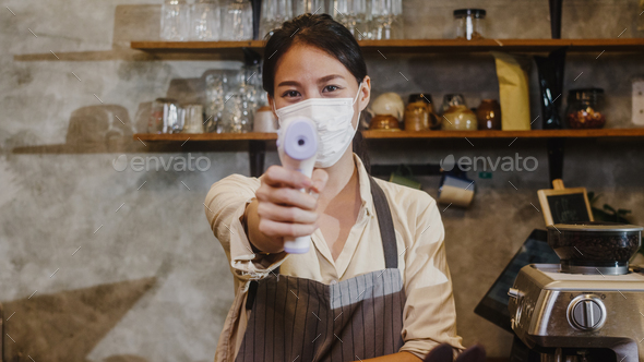Young Asia female restaurant wearing protective face mask using infrared thermometer checker.