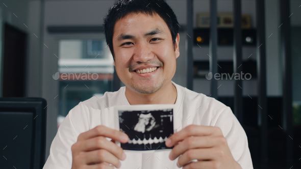Portrait Asian Chinese man show and looking ultrasound photo baby in his wife at home. - Stock Photo - Images