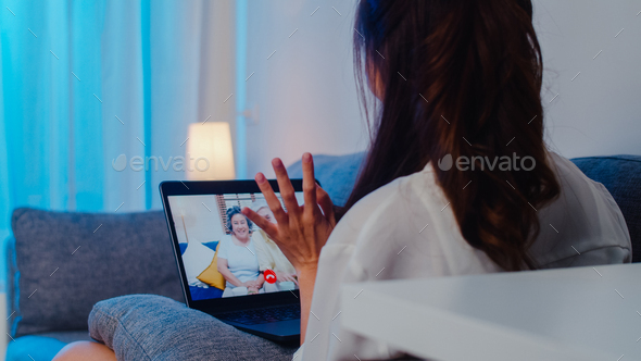 Asia student exchange female using laptop video call talking with family at living room at night.