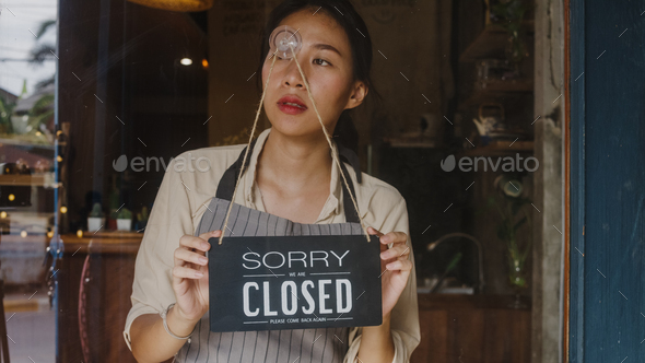 Young Asia manager girl turning a sign from open to closed sign on glass door cafe.