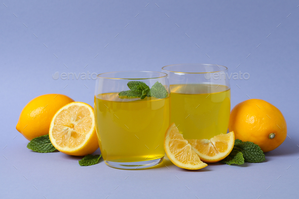 Glasses of lemon jelly, lemon slices and mint on violet background