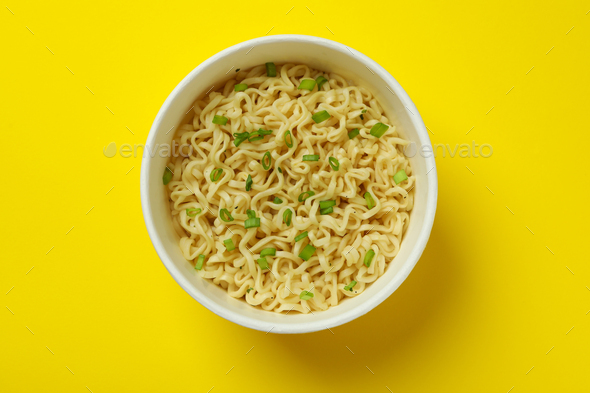 Cooked instant noodles in paper cup on yellow background