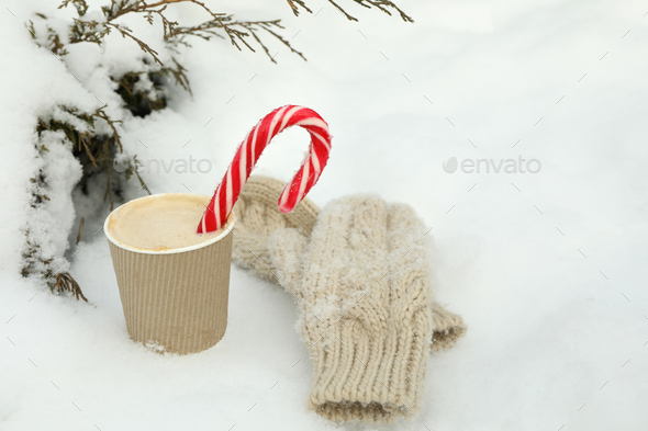 Paper cup with coffee and candy canes and mittens outdoor in winter
