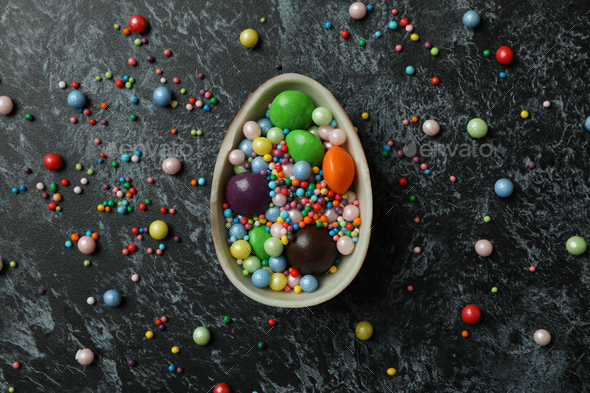 Half of chocolate egg with candies and sprinkles on black smokey background