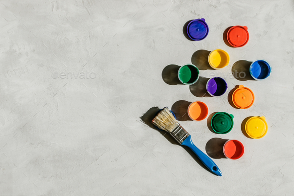 Action painting, trend art background. Multicolored paints in round jars and brush on a gray