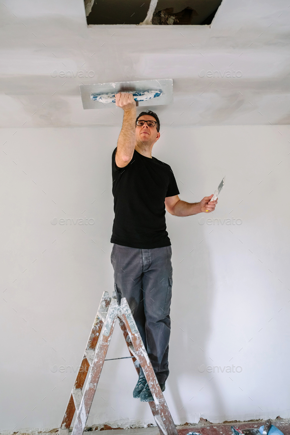 Plasterer smoothing plaster ceiling with the trowel Stock Photo by