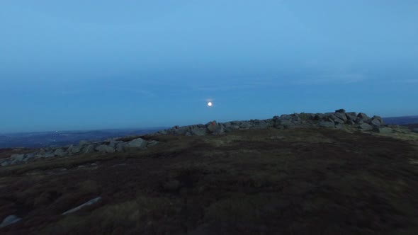 Aerial shot of men climbing boulders while bouldering at night under a full moon. alt