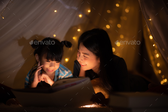 young Asian mother read the story in the book for her daughter children on the bed at home