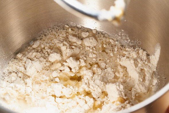 Raw yeast dough mixing in large metal bowl in mixer. Flour, water and yeast mixing