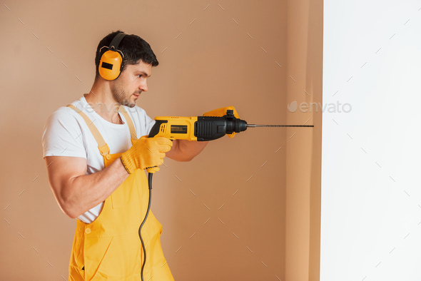 Handyman in yellow uniform works indoors by using hammer drill. House renovation conception