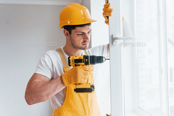 Handyman In Yellow Uniform Installs New Window By Using Automatic Screwdriver Stock Photo By Mstandret