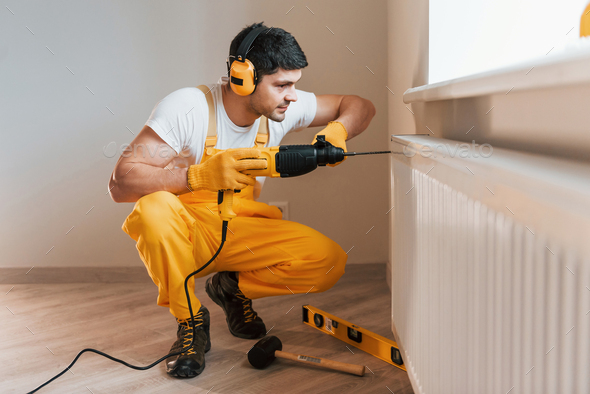 Handyman in yellow uniform works indoors by using hammer drill. House renovation conception