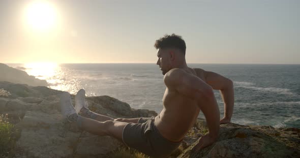 Man with naked torso doing triceps exercises on rocky shore alt