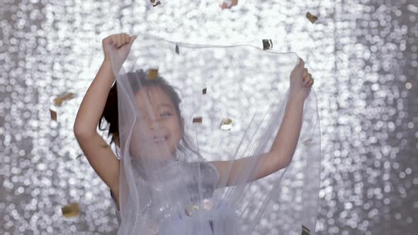 Cute Happy Little Girl Child in a Silver Dress Dancing on Background of Silver Bokeh.