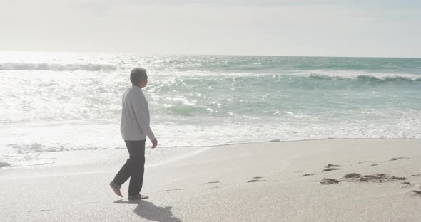 Side view of hispanic senior man walking on beach at sunset alt