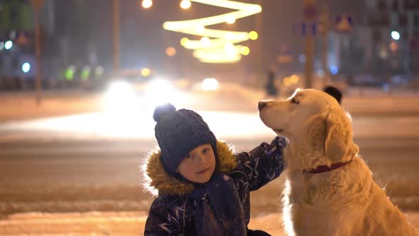 Love for Pets. Little Boy Stroking His Dog Outdoors in Winter in the Evening City