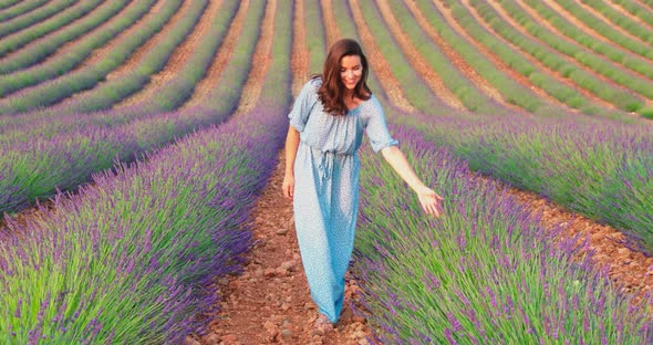 The Beautiful Young Girl Walks Across the Field of a Lavender at Sunset She is Wearing a Long Blue alt