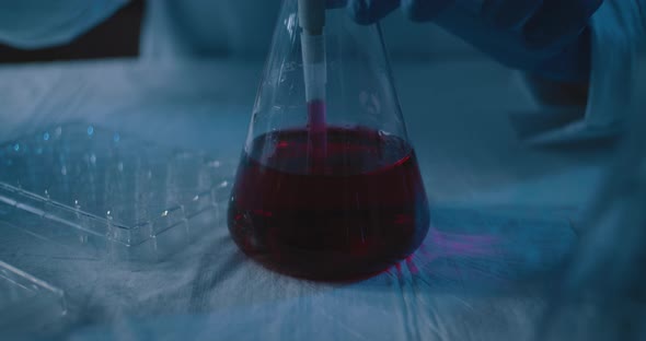 Scientist taking out a red liquid from a conical flask and placing it into plate alt