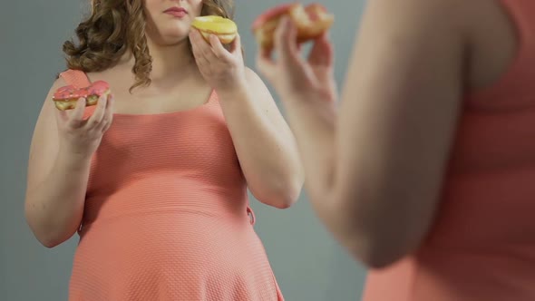 Sad Fat Girl Crying at Her Reflection in Mirror, Eating Two Donuts at Same Time alt