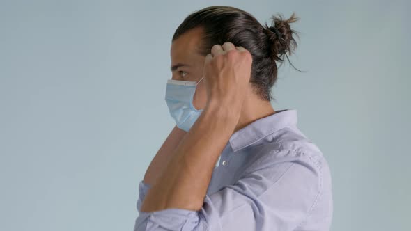 Left side shot of handsome man putting on hygienic mask. Static, bluish background alt