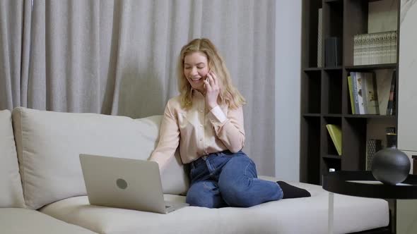 Young adult woman typing on a laptop talking on the phone alt