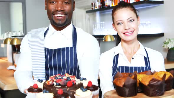 Portrait of smiling waiter and waitress presenting desserts at counter alt