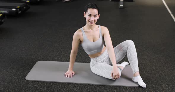 A Young Athletic Woman is Resting After Doing Exercises Sitting on the Mat in the Gym Dressed in