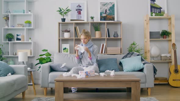 Girl with a Cold Sneezes While Sitting on a Couch in a Living Room alt