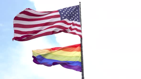 American flag and the rainbow LGBT pride gay pride flag waving in the wind with blue sky and clouds alt