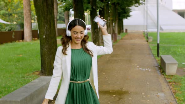 Woman with coffee cup dancing in park wearing headphones