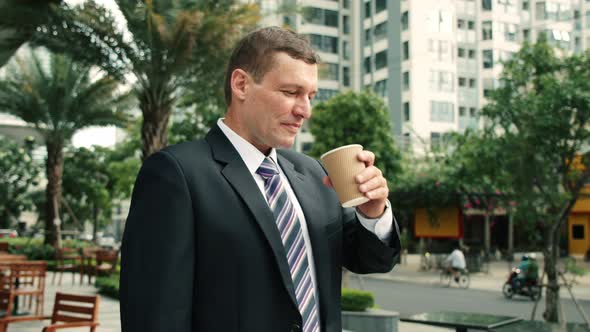The Shot Moves Around a Businessman Standing on Street in the City Center Who and Drinks Hot alt
